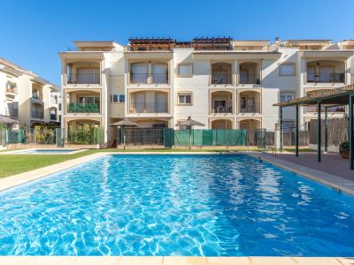Amplia piscina comunitaria de agua salada, rodeada de césped verde y edificios de apartamentos color crema con balcones privados.