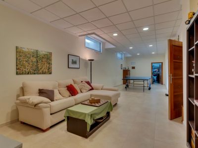 Amplia sala de estar en planta inferior con sofá en L, mesa de centro, mesa de ping-pong y ventanas altas, ideal como zona de juegos o segundo salón.