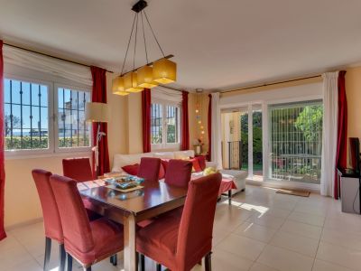 Amplio salón-comedor con mesa de madera para seis, sillas tapizadas en rojo y abundante luz natural. Acceso directo al jardín y ventanales con rejas de seguridad.