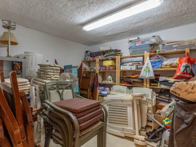 Amplio trastero con estanterías de madera repletas de objetos domésticos, muebles de jardín apilados y una luminaria fluorescente en el techo.