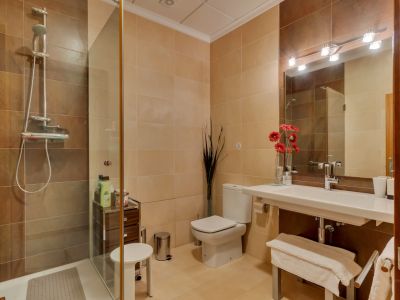 Baño completo con ducha acristalada, azulejos en tonos beige y marrón, lavabo suspendido y espejo con iluminación moderna.