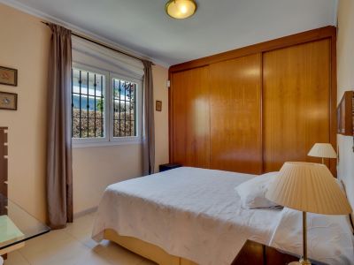 Dormitorio con cama doble, armario empotrado de madera y ventana con rejas que da a vegetación exterior.