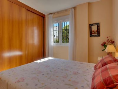 Dormitorio principal con amplio armario empotrado de madera clara, cama doble y ventana con rejas que ofrece luz natural y vistas a la vegetación.