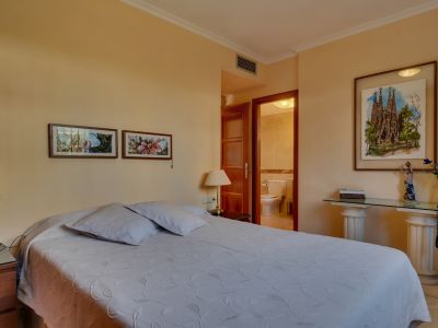 Dormitorio principal con cama doble, mesitas de noche de madera y acceso directo a un baño privado. Destacan cuadros decorativos y una consola de cristal con pilares clásicos.