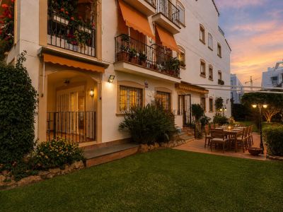 Jardín privado con césped y patio embaldosado, ideal para cenas al aire libre. Destaca la mesa de comedor de madera, la iluminación ambiental y la exuberante vegetación al atardecer.