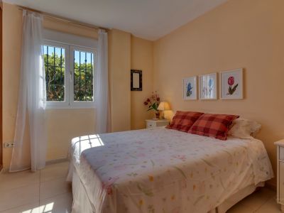 Luminoso dormitorio con paredes color melocotón, cama doble, y ventana con rejas que ofrece vistas al jardín y abundante luz natural. Incluye armario empotrado.
