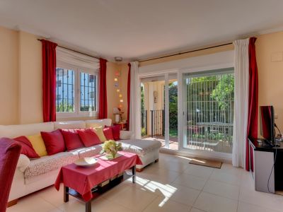 Salón luminoso con sofá blanco, cojines vibrantes, suelo de baldosas y acceso directo al jardín privado a través de puertas correderas.