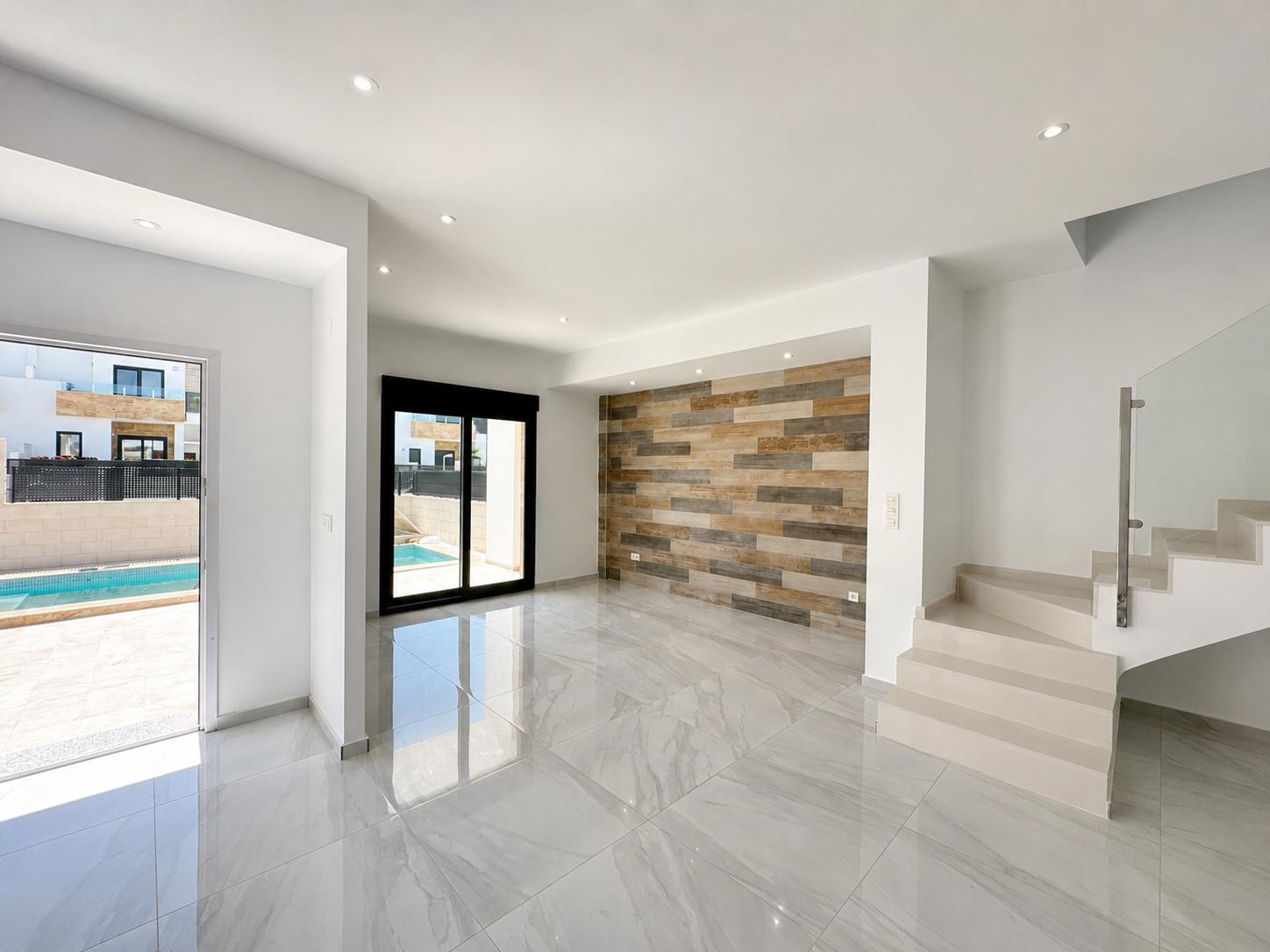 Amplia sala de estar con suelo porcelánico, pared decorativa de paneles efecto madera y acceso directo a la piscina privada. Escalera moderna con barandilla de cristal.
