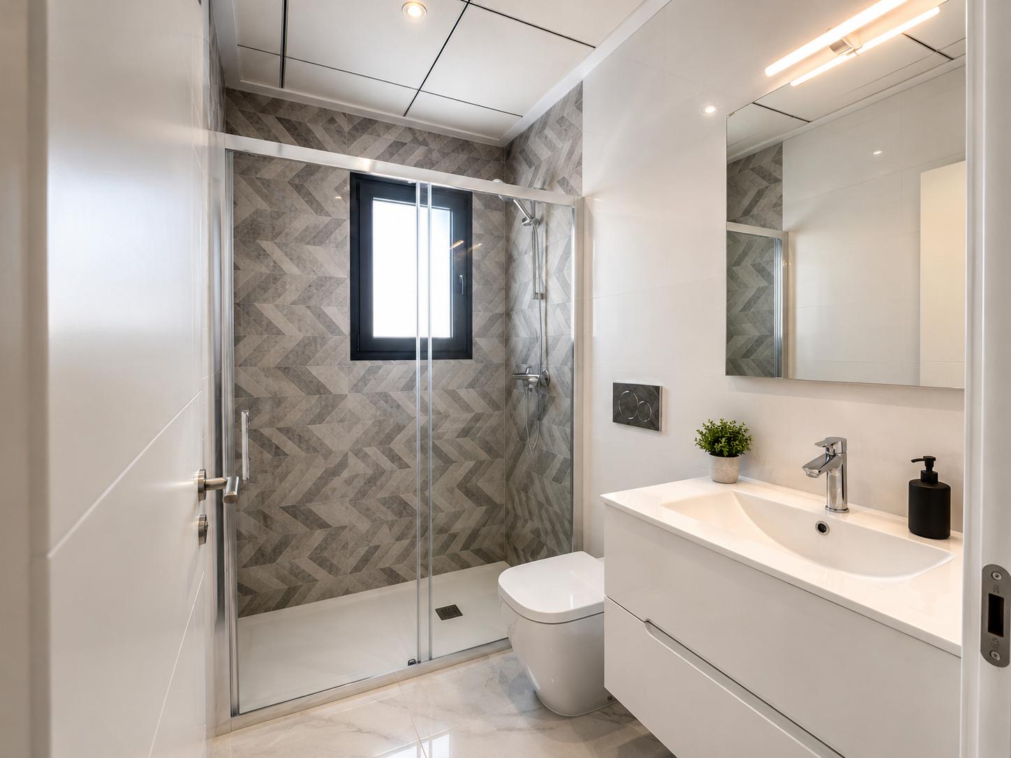 Baño contemporáneo con ducha de obra, mampara de cristal, azulejos geométricos grises en la pared y ventana. Lavabo flotante blanco sobre suelo de mármol.