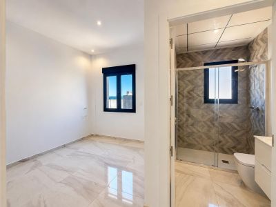 Amplio dormitorio con suelo de efecto mármol claro y ventana oscura con vistas lejanas, colindante con baño en suite de ducha y paredes con azulejos geométricos.