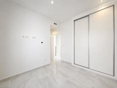 Habitación moderna con amplios armarios empotrados blancos de puertas correderas, suelo de gres porcelánico efecto mármol y focos empotrados en el techo. Un diseño limpio y funcional.