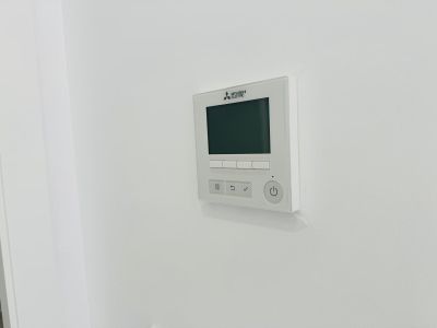 Panel de control Mitsubishi Electric para aire acondicionado por conductos, con pantalla digital y botones intuitivos, integrado en la pared blanca.