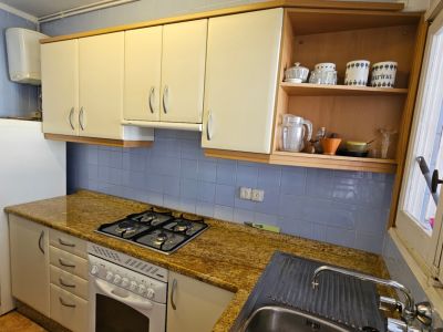 Cocina funcional con azulejos azules, encimera de granito moteado y mobiliario en tonos crema. Incluye placa de gas, horno y fregadero de acero, con luz natural de la ventana.