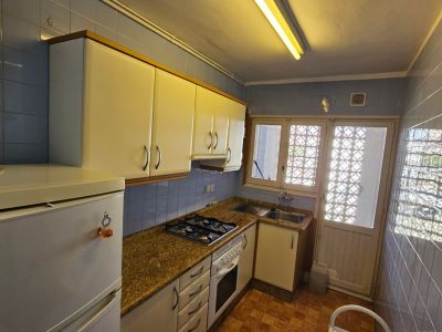 Cocina funcional con azulejos azules, encimera de granito y armarios blancos. Dispone de horno, fogones de gas y luz natural a través de una ventana con celosía.