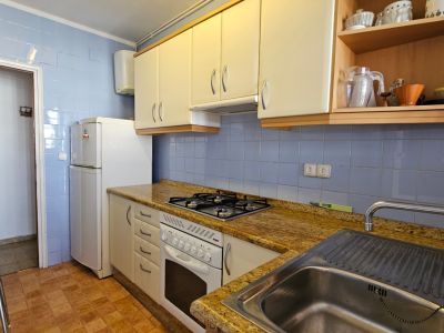 Cocina funcional con azulejos azules, encimera efecto granito y armarios blancos. Equipada con placa de gas, horno, fregadero de acero inoxidable y nevera.