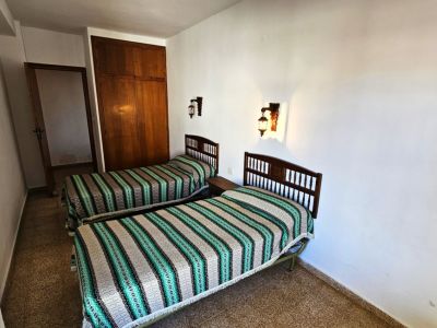 Dormitorio con dos camas individuales de cabecero de madera y colchas a rayas. Incluye armario empotrado de madera y apliques de pared, sobre un suelo de gres.