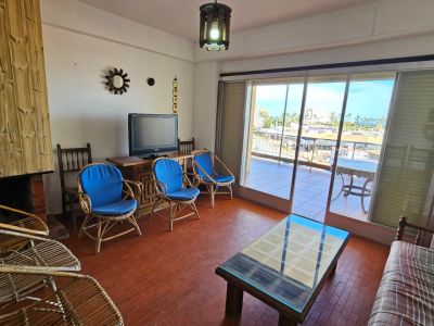 Sala de estar con suelo de terracota, chimenea con revestimiento de madera vertical y mobiliario de mimbre. Amplias puertas correderas dan a una terraza exterior con vistas urbanas.