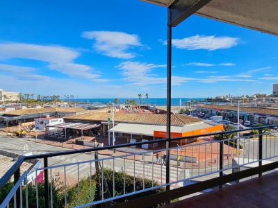 Vista desde la terraza sobre una calle animada con comercios y tejados de teja, extendiéndose hacia la Playa del Arenal y el azul claro del Mediterráneo bajo un cielo brillante.