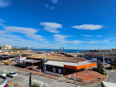 Vista elevada a la Playa del Arenal y el Mediterráneo, con tejados de terracota, palmeras y la vida urbana de Jávea en primer plano.