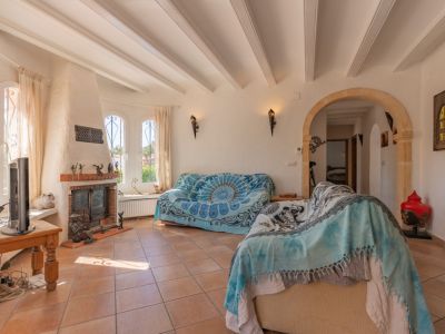 Luminoso salón con una chimenea tradicional de ladrillo, ventanas arqueadas con rejas y techo con vigas vistas. El suelo es de baldosas de terracota, y un arco de piedra decorativo conecta con el interior.