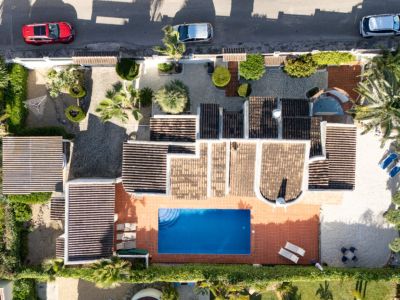 Vista aérea de la villa privada con piscina rectangular azul, terraza solárium de baldosas de terracota y amplio jardín con árboles mediterráneos y entrada pavimentada.
