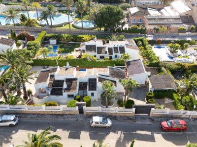 Vista aérea de la villa privada en Jávea, mostrando su fachada blanca, tejados oscuros, una gran piscina y un exuberante jardín mediterráneo con palmeras y entrada privada.