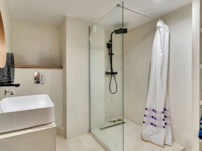 Baño moderno con lavabo sobre encimera, grifería negra mate y ducha a ras de suelo con mampara de cristal. Destacan el espejo de madera y estantes integrados.