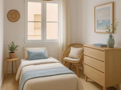 Dormitorio individual con cama en tonos neutros y azul. Destacan el mobiliario de madera clara y ratán, la lámpara colgante de mimbre y la luz natural.