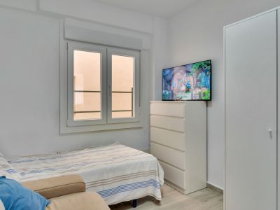 Dormitorio secundario con cama individual, armario empotrado blanco y cómoda con TV. La ventana de doble hoja proporciona luz natural.