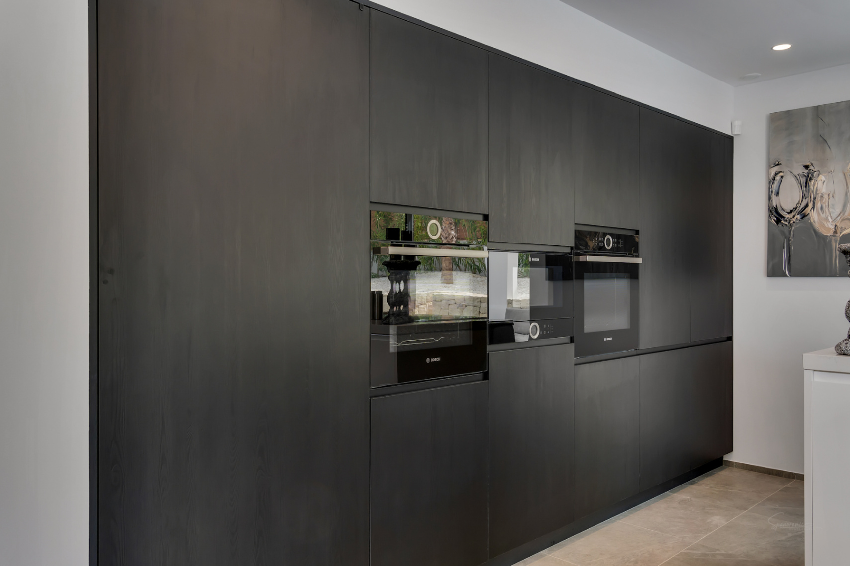 Cocina de diseño con cabinetry oscuro de textura amaderada, integrando electrodomésticos Bosch modernos. Las puertas de los hornos reflejan sutilmente el exterior.