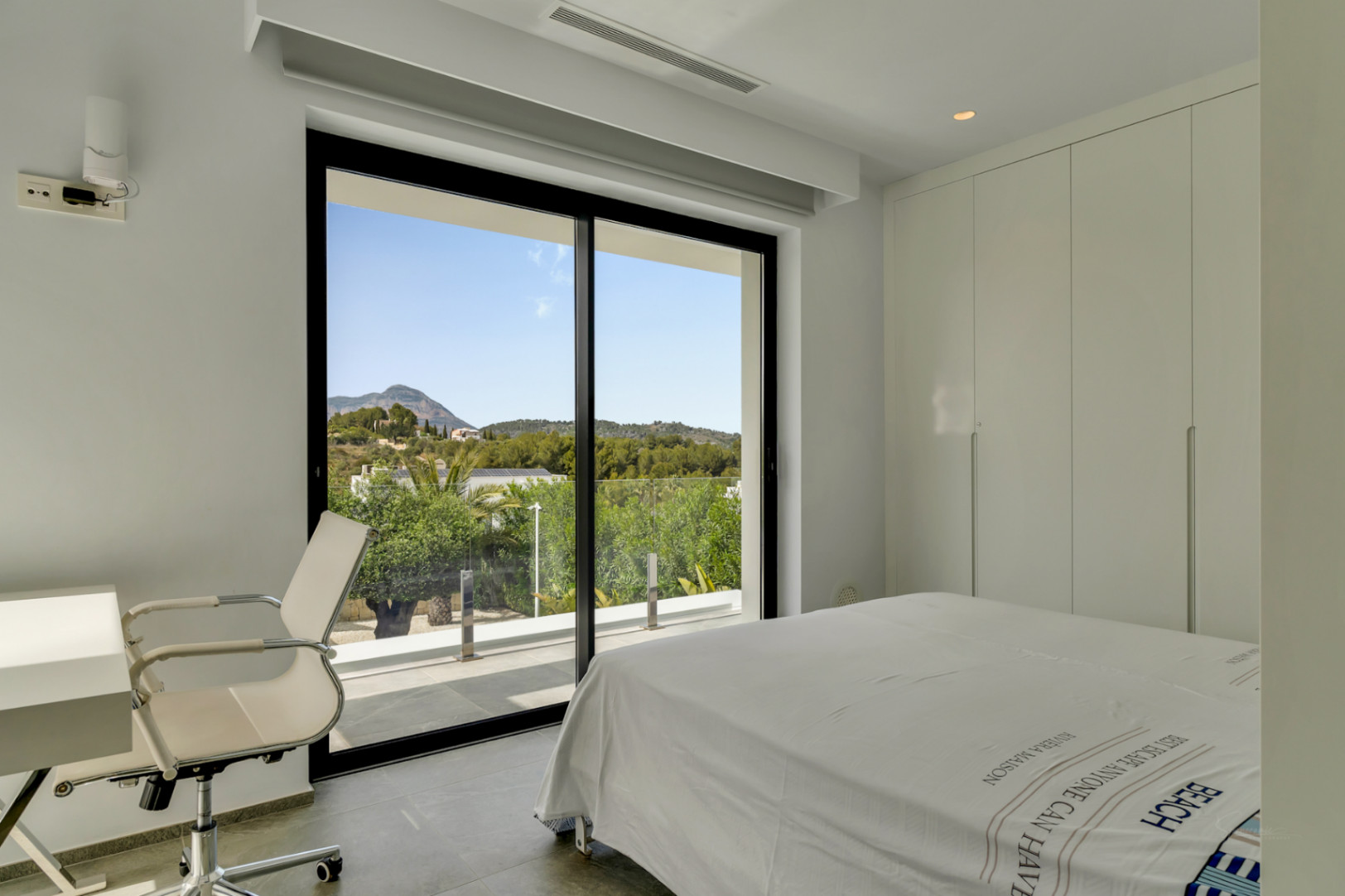 Dormitorio moderno con amplias puertas de cristal, acceso directo a la terraza y vistas panorámicas a las verdes montañas. Incluye armarios empotrados y un espacio de trabajo.