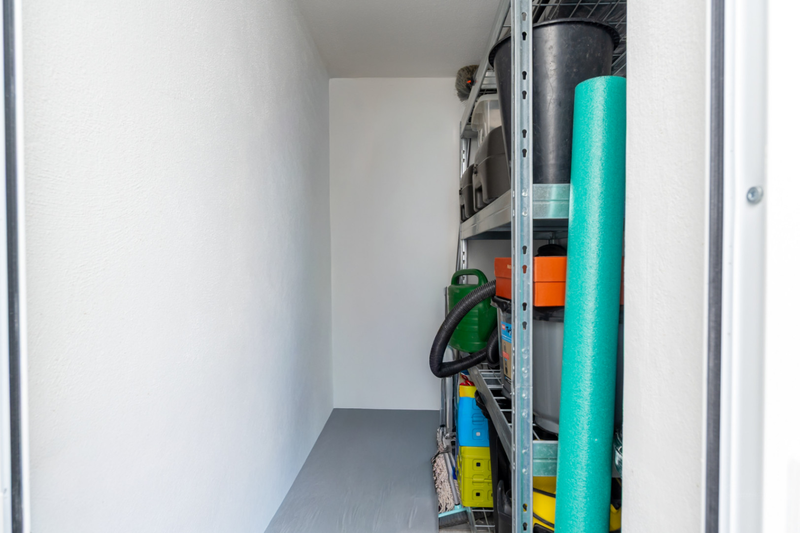 Espacio de almacenamiento funcional con paredes blancas, suelo gris y estanterías metálicas robustas, ideal para organizar enseres.