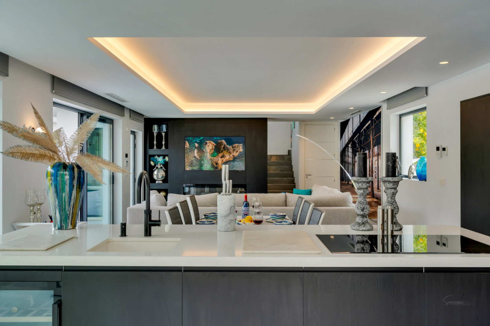 La isla de cocina de concepto abierto, con encimera blanca y placa integrada, conecta el comedor y la sala de estar, realzada por iluminación indirecta.