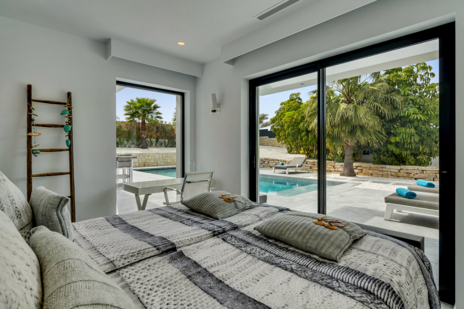 Luminoso dormitorio con acceso directo a la piscina privada y tumbonas a través de amplias puertas correderas de cristal. Diseño moderno con paredes blancas y luz natural.