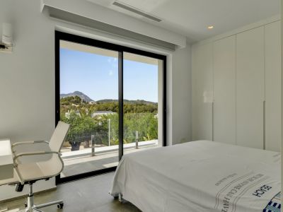 Dormitorio moderno con amplias puertas de cristal, acceso directo a la terraza y vistas panorámicas a las verdes montañas. Incluye armarios empotrados y un espacio de trabajo.