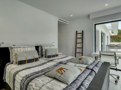 Dormitorio principal moderno con cama doble, escritorio integrado y acceso directo a una terraza exterior, iluminado por luz natural y focos empotrados.