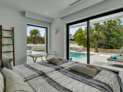 Luminoso dormitorio con acceso directo a la piscina privada y tumbonas a través de amplias puertas correderas de cristal. Diseño moderno con paredes blancas y luz natural.