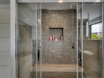 Moderna ducha doble con azulejos de efecto piedra gris, dos rociadores de lluvia y un asiento integrado. Incluye un nicho empotrado y vistas parciales al exterior.