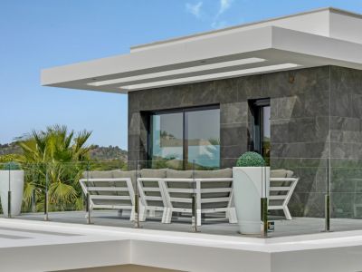 Terraza exterior con mobiliario moderno de diseño, barandilla de cristal y fachada de azulejos grises. Vistas a la vegetación y colinas.