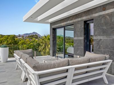 Terraza exterior con mobiliario moderno, suelo de gres y pared de azulejos oscuros. Vistas a la montaña y vegetación, con acceso directo a una habitación interior.