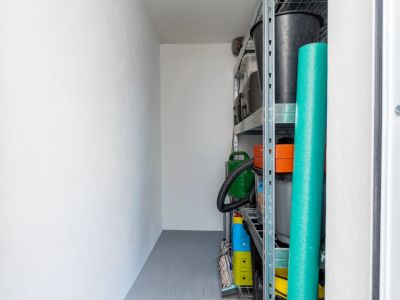 Trastero bien organizado con estanterías metálicas robustas que contienen diversos artículos domésticos y de jardín, sobre paredes blancas y suelo gris.
