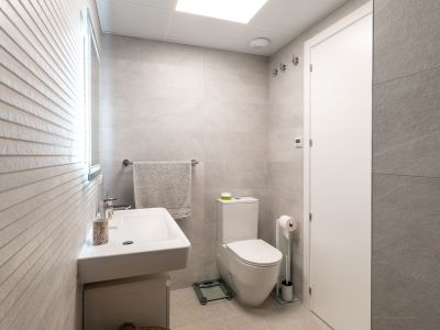 Baño moderno con azulejos grises de gran formato, lavabo suspendido y espejo iluminado. Una pared de acento presenta un diseño texturizado horizontal.
