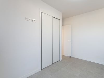 Dormitorio con amplio armario empotrado de puertas correderas blancas y suelo de gres claro. Incluye tomas eléctricas y de datos modernas.