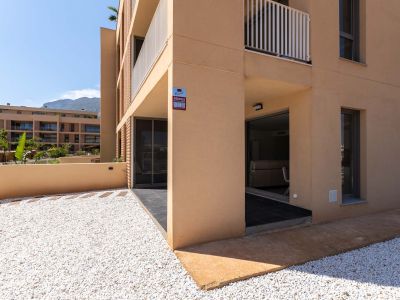 Exterior de planta baja con fachada moderna color ocre. Destaca un jardín privado de grava blanca y terraza cubierta con acceso directo al interior, con vistas a la montaña.