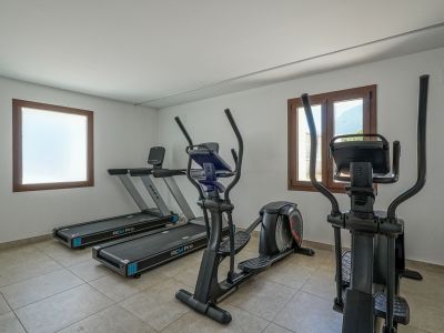Gimnasio residencial equipado con dos cintas de correr BH RCM Pro y dos elípticas. Cuenta con suelo de gres, paredes blancas y ventanas con marcos de madera, una con vistas a la montaña.