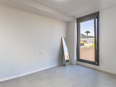 Habitación vacía con paredes blancas y suelo de gres gris, lista para personalizar. Gran ventanal con vistas a una palmera y montañas, aportando abundante luz natural.