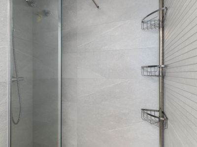 Moderna zona de ducha con azulejos grises de gran formato, una pared de acento texturizada, mampara de cristal y una práctica estantería esquinera cromada.