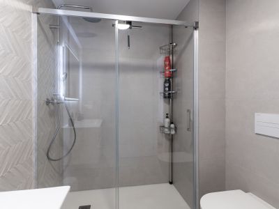 Moderno baño con cabina de ducha de cristal y plato blanco. Destacan los azulejos grises con patrón de espiga, ducha de lluvia y un inodoro suspendido.