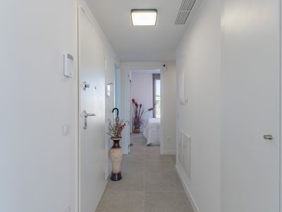Pasillo moderno y luminoso con suelo de gres claro y paredes blancas. Incluye panel de seguridad, iluminación de techo contemporánea y vista a un dormitorio.