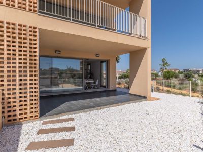 Terraza cubierta de planta baja con baldosas oscuras, conectada a un jardín privado de grava blanca. Grandes puertas de cristal revelan un luminoso comedor interior, junto a una moderna fachada con celosía de ladrillo.